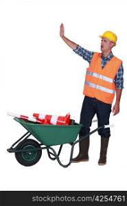 Builder making stop gesture whilst stood with traffic cones