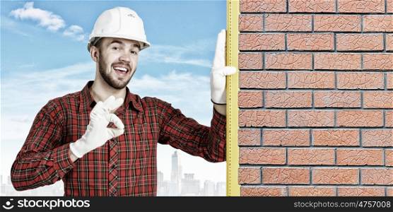 Builder man with level. Bricklayer using level to check new red brick wall outdoor