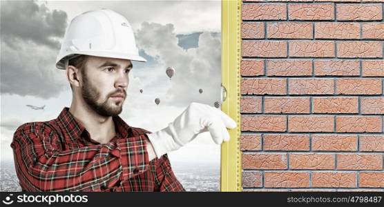 Builder man with level. Bricklayer using level to check new red brick wall outdoor