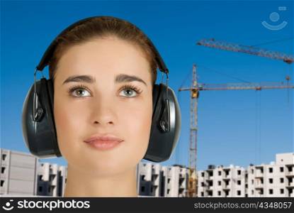 Builder pretty girl at safety earphone on a building background