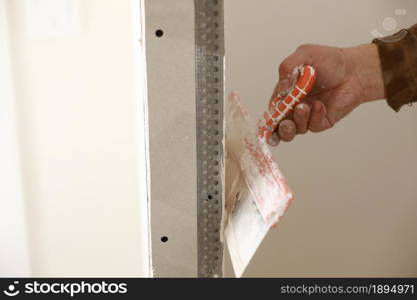 Builder using a trowel to add plaster. Plastering wall with putty-knife, close up image. Fixing wall surface and preparation for painting. construction work during quarantine.. Builder using a trowel to add plaster. Plastering wall with putty-knife, close up image. Fixing wall surface and preparation for painting. construction work during quarantine