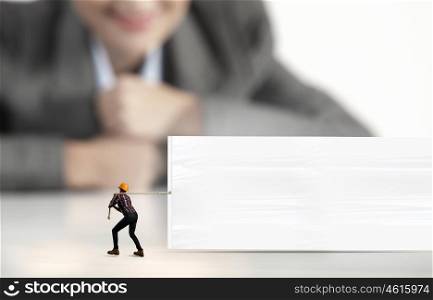 Builder with banner. Businesswoman looking at miniature of builder pulling white banner