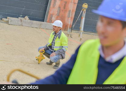 builder with theodolite transit equipment at construction site outdoors