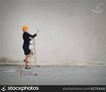 Builder woman on ladder. Attractive engineer woman with paint roll climbing ladder
