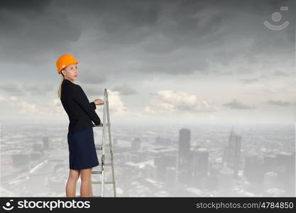 Builder woman viewing city. Attractive engineer woman climbing ladder high above city