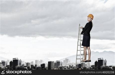 Builder woman viewing city. Attractive engineer woman climbing ladder high above city