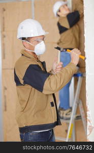 builders working indoors man in foreground using hammer and chisel