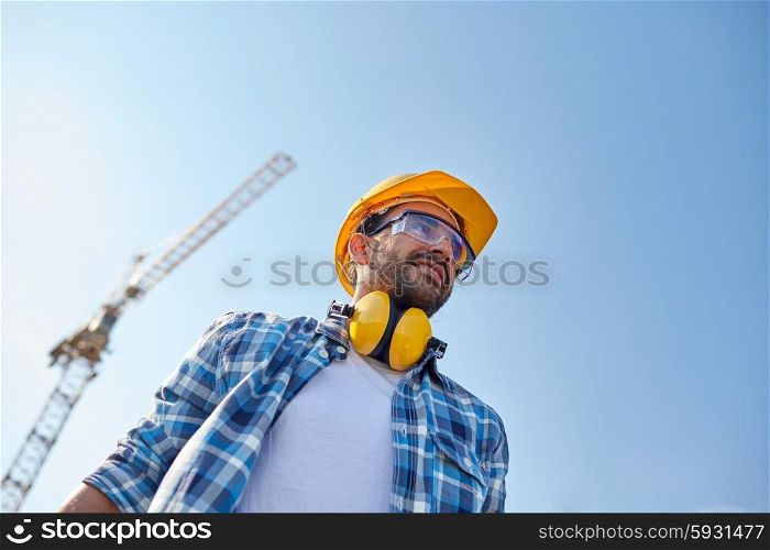building and people concept - smiling builder with hardhat and headphones over blue sky and construction crane. smiling builder with hardhat and headphones