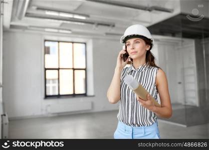 building, architecture and construction business concept - businesswoman or architect in helmet with blueprint calling on smartphone at office room. architect with blueprint calling on cell at office