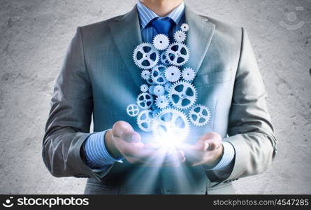 Building business. Close up of businessman holding gears in palms