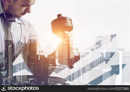 Building business muscles. Hard working business concept. Strong businessman with dumbbell mixed with sunset city skyline
