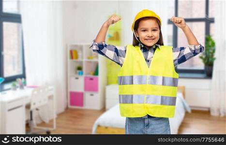 building, construction and girl power concept - smiling little girl in protective helmet and safety vest showing her strong arms over children&rsquo;s room at home background. girl in helmet and safety vest showing power