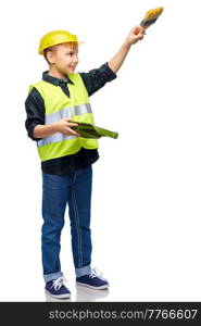 building, construction and profession concept - happy smiling little boy in protective helmet and safety vest with brush and tray painting something imaginary over white background. little boy in protective helmet with brush