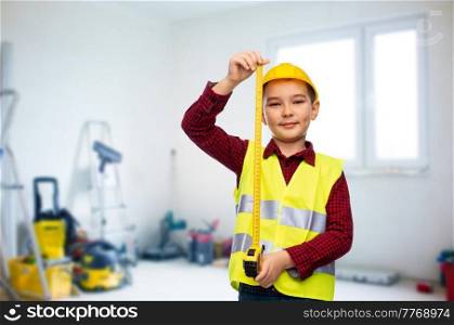 building, construction and profession concept - little boy in protective helmet and safety vest with ruler over room with working equipment background. boy in construction helmet and vest with ruler