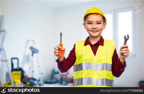 building, construction and profession concept - little boy in protective helmet and safety vest holding screwdriver and wrench over room with working equipment background. boy in building helmet with screwdriver and wrench
