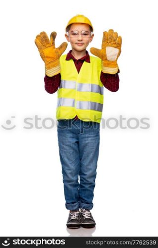 building, construction and profession concept - little boy in protective helmet, gloves, goggles and safety vest over white background. boy in protective helmet, gloves and safety vest