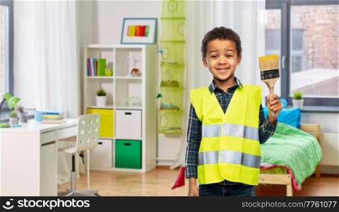 building, construction and profession concept - little boy in safety vest with paint brush over children’s room background. boy in safety vest with paint brush at home