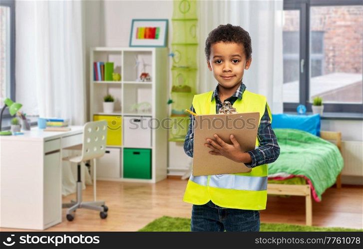 building, construction and profession concept - little boy in safety vest with clipboard over children&rsquo;s room background. little boy in safety vest with clipboard at home