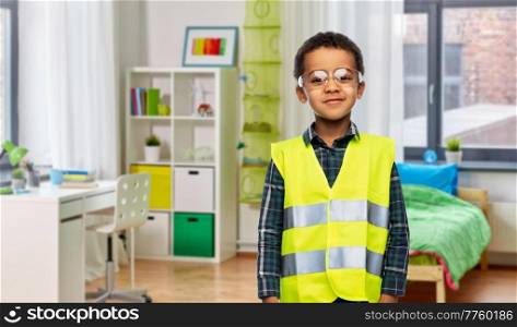 building, construction and profession concept - smiling little boy in goggles and yellow safety vest over children’s room background. little boy in goggles and safety vest at home