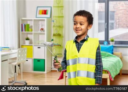 building, construction and profession concept - smiling little boy in yellow safety vest with paint roller over children’s room background. boy in safety vest with paint roller at home