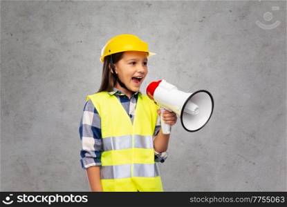 building, construction and profession concept - smiling little girl in protective helmet and safety talking to megaphone vest over grey concrete wall background. little girl in helmet talking to megaphone