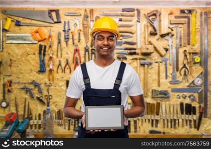 building, construction and technology concept - happy smiling indian worker or builder in helmet with tablet pc computer over work tools on background. happy indian builder in helmet with tablet pc