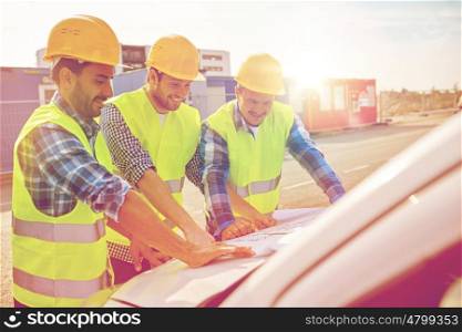 building, construction, development, teamwork and people concept - close up of builders in hardhats and high visible vests with blueprint on car hood