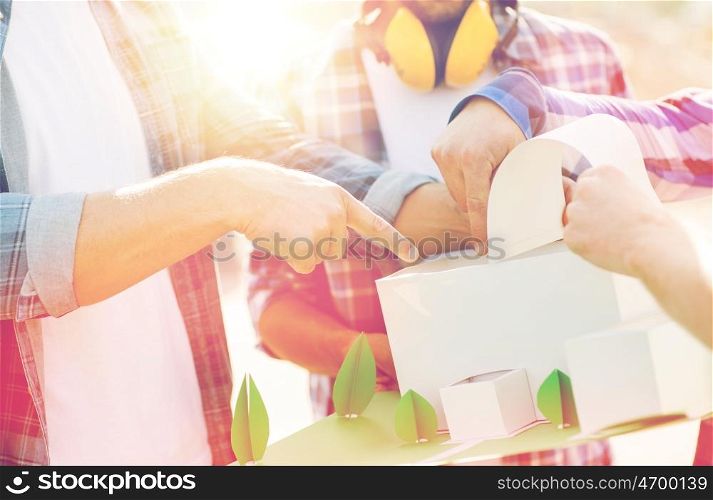 building, construction, teamwork and people concept - close up of builders hands with paper house model or layout outdoors