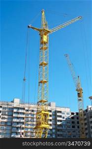 Building crane and building under construction on blue cloudy sky