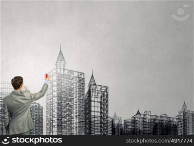 Building design. Back view of businessman drawing sketches of construction project on wall