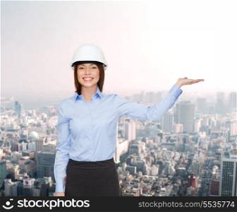 building, developing, advertising and architecture concept - friendly young smiling businesswoman in white helmet holding something on palm