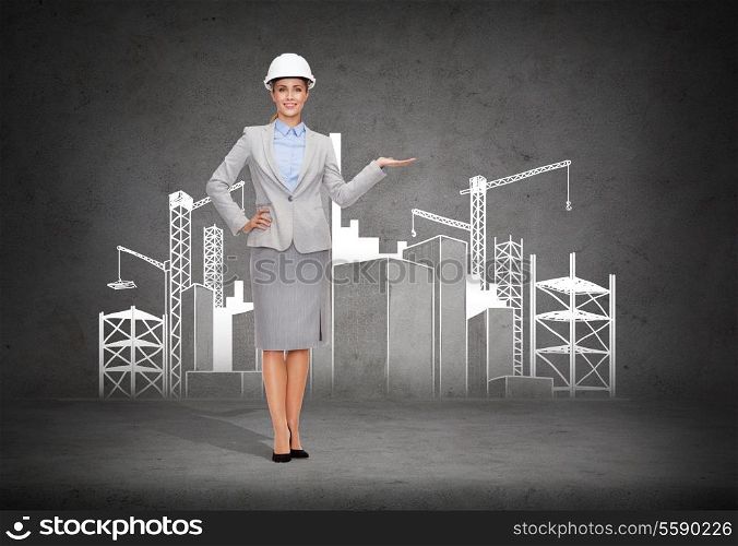 building, developing, advertising and architecture concept - friendly young smiling businesswoman in white helmet showing construction site