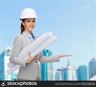 building, developing, consrtuction and architecture concept - smiling architect in helmet with blueprints showing something on palm of hand