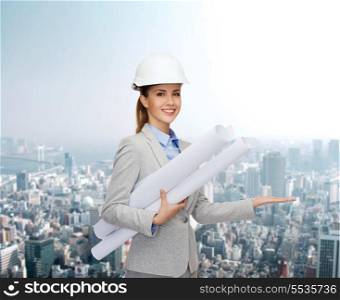 building, developing, consrtuction and architecture concept - smiling architect in helmet with blueprints showing something on palm of hand