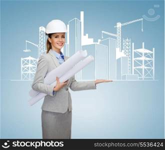 building, developing, consrtuction and architecture concept - smiling architect in helmet with blueprints showing city sketching on palm of hand