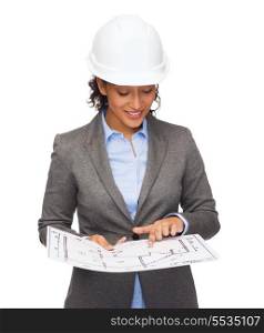 building, developing, consrtuction and architecture concept - smiling businesswoman in white helmet pointing finger to blueprint