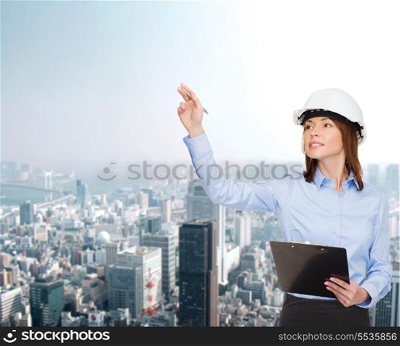 building, developing, consrtuction and architecture concept - smiling businesswoman in white helmet with clipboard pointing finger