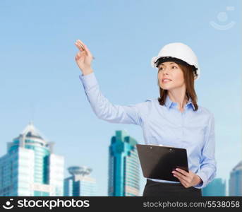 building, developing, consrtuction and architecture concept - smiling businesswoman in white helmet with clipboard pointing finger