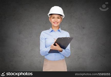 building, developing, construction and architecture concept - smiling businesswoman in helmet with clipboard in front of the concrete wall