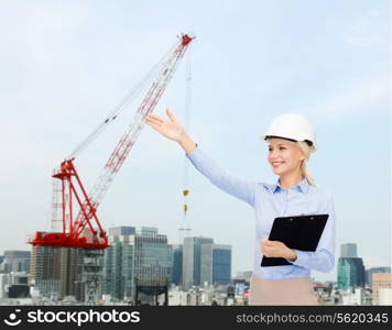 building, developing, construction and architecture concept - smiling businesswoman in white helmet with clipboard over city building background