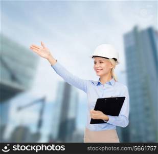 building, developing, construction and architecture concept - smiling businesswoman in white helmet with clipboard over city background