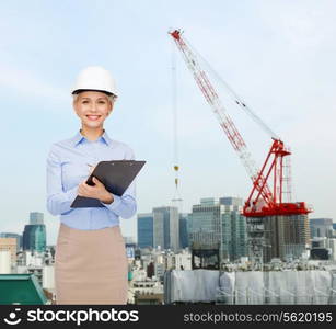 building, developing, construction and architecture concept - smiling businesswoman in white helmet with clipboard making notes