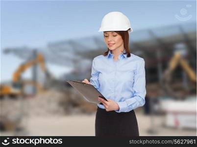 building, developing, construction and architecture concept - smiling businesswoman in white helmet with clipboard making notes