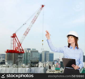 building, developing, construction and architecture concept - smiling businesswoman in white helmet with clipboard pointing finger