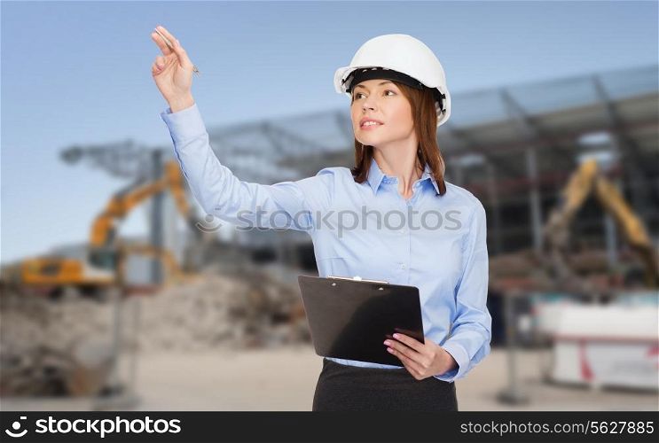 building, developing, construction and architecture concept - smiling businesswoman in white helmet with clipboard pointing finger