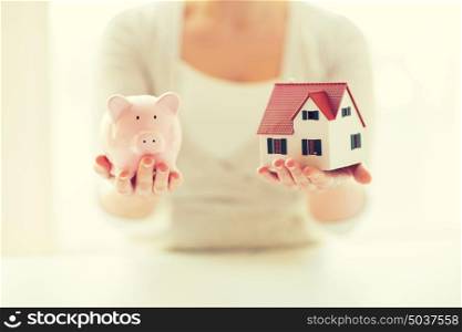 building, mortgage, investment, real estate and property concept - close up of woman holding home or house model and piggy bank. close up of woman with house model and piggy bank