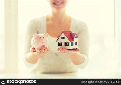 building, mortgage, investment, real estate and property concept - close up of woman holding home or house model and piggy bank. close up of woman with house model and piggy bank