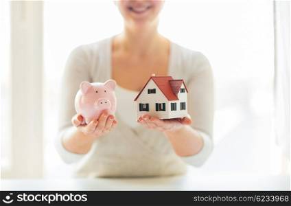 building, mortgage, investment, real estate and property concept - close up of woman holding home or house model and piggy bank