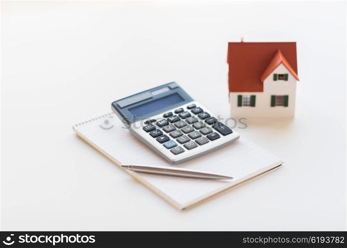 building, mortgage, real estate and property concept - close up of home model, house keys and notebook with pen