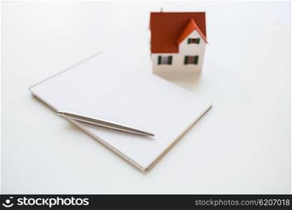 building, mortgage, real estate and property concept - close up of house model, notebook and pencil